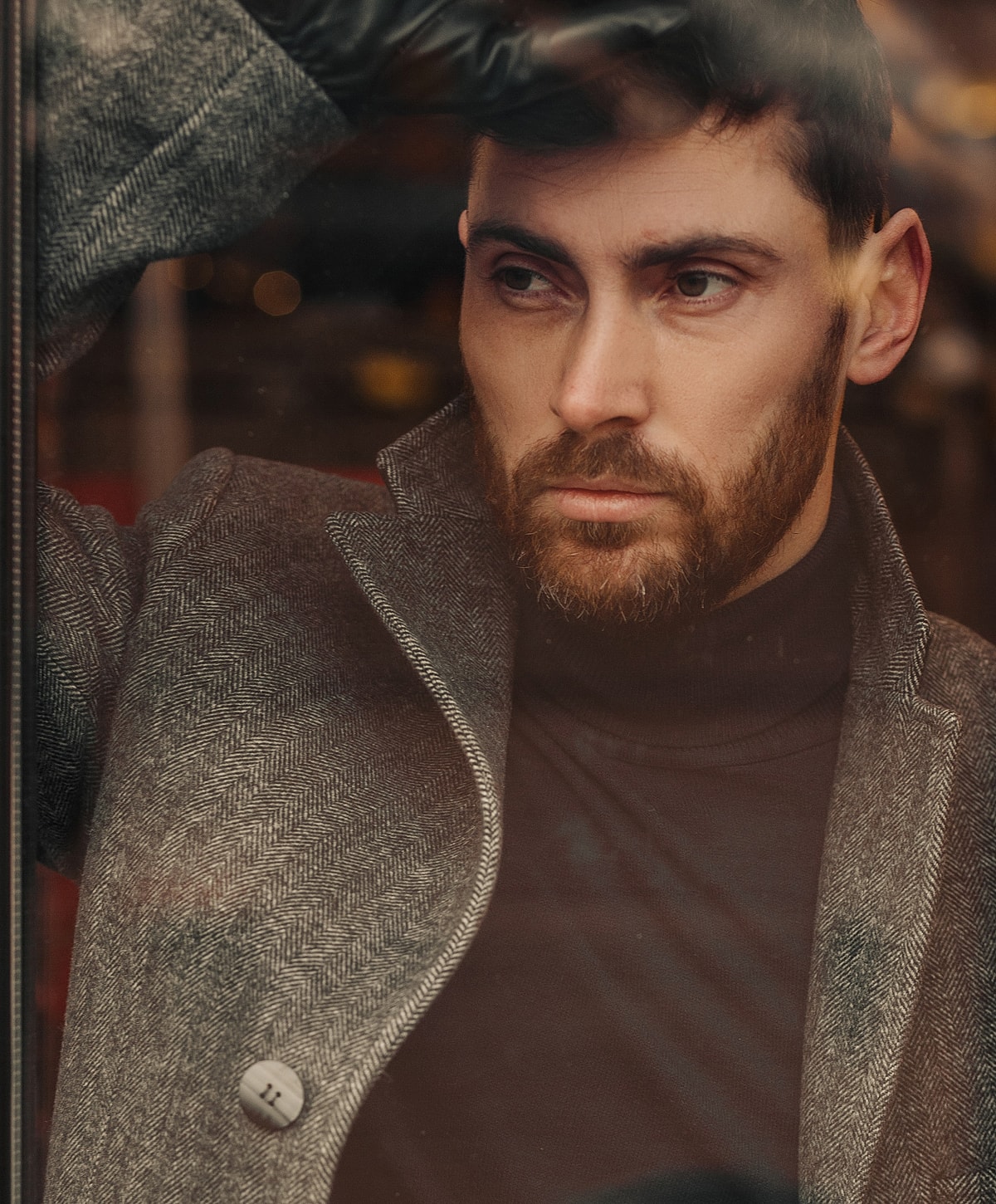 Man in stylish coat gazing thoughtfully outside.